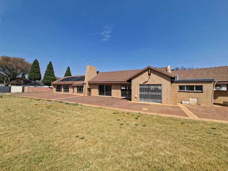 Rear view of a single-story brick house featuring a large paved patio area, solar panels, and a spacious lawn.