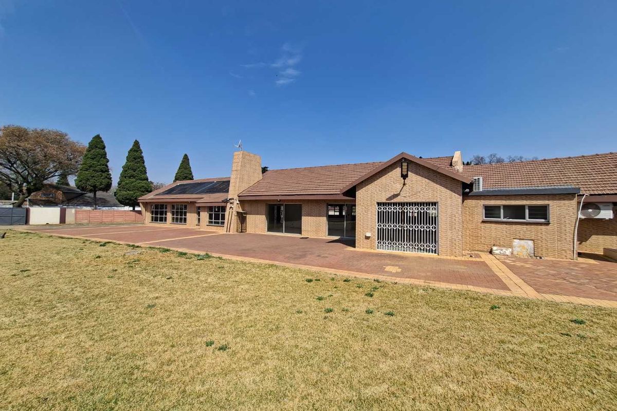 Rear view of a single-story brick house featuring a large paved patio area, solar panels, and a spacious lawn.