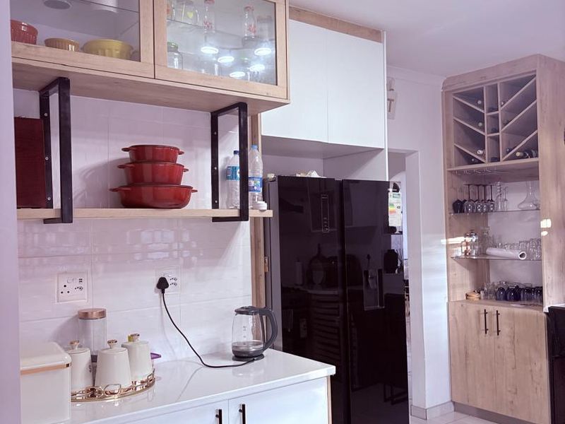 Modern kitchen featuring light wood-tone cabinetry, glass-fronted display units, a dedicated wine rack, and a clean tiled backsplash with contemporary finishes.