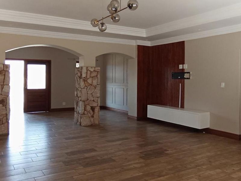 Spacious living area featuring stone-clad pillars, wood-panelled accent wall, crown molding, and modern tiled flooring, offering a bright and open layout.