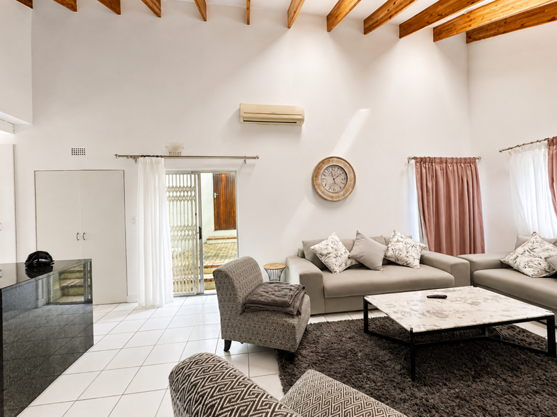 Spacious living room featuring high ceilings with exposed timber beams, tiled flooring, and direct access to an outdoor area through a sliding glass door.