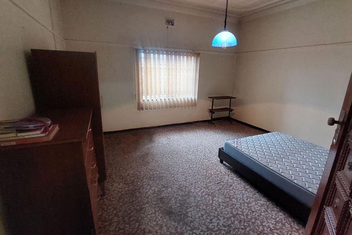 A bedroom featuring patterned carpeting, a window with vertical blinds, and a ceiling-mounted light fixture.