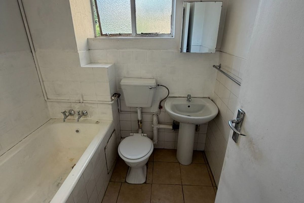 A compact bathroom featuring a standard bathtub, pedestal basin, and toilet with tiled finishes, requiring cosmetic updates to improve its overall condition.