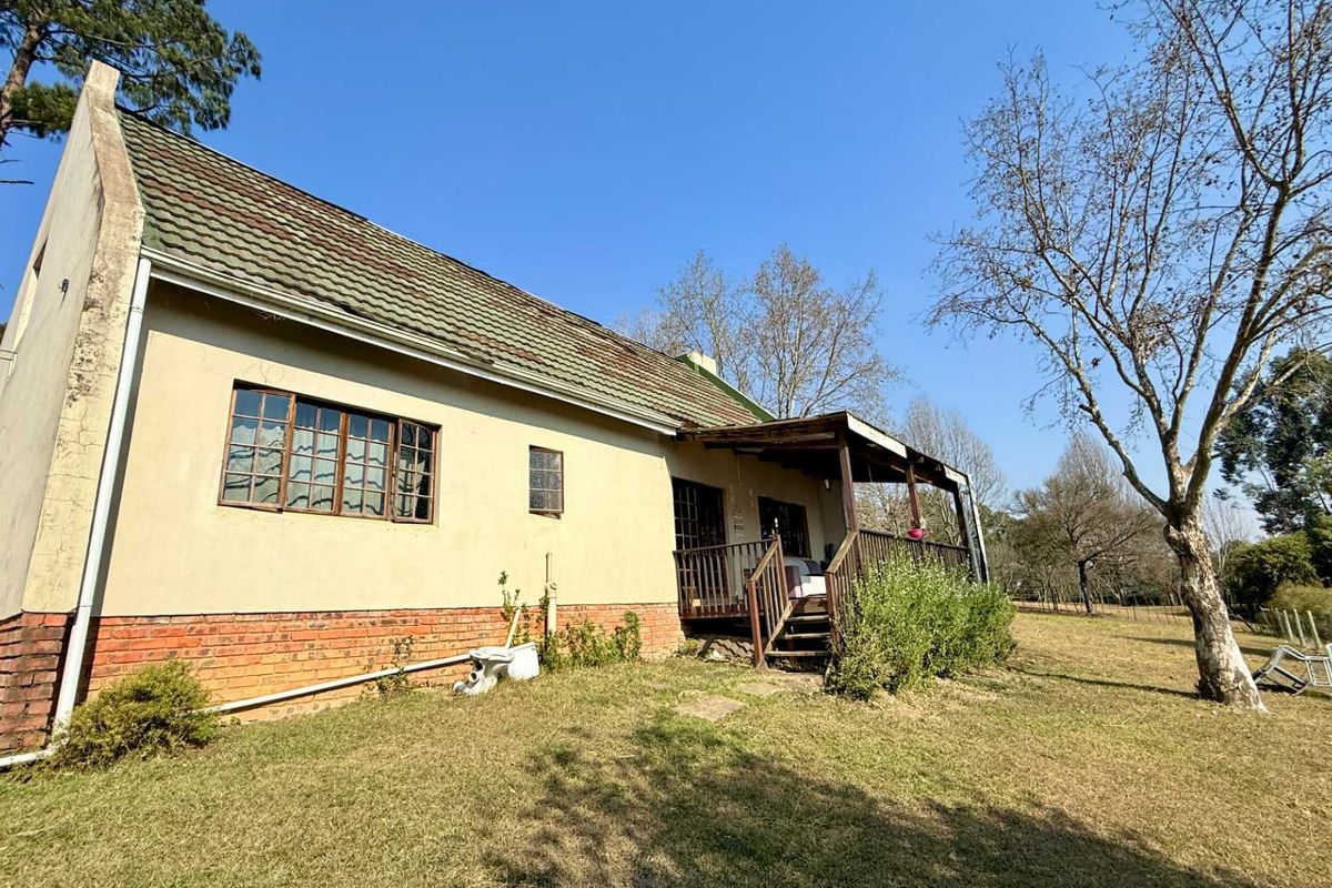 Rear view of a farm-style dwelling featuring a timber deck, brick base, and tiled roof set within a spacious rural garden.