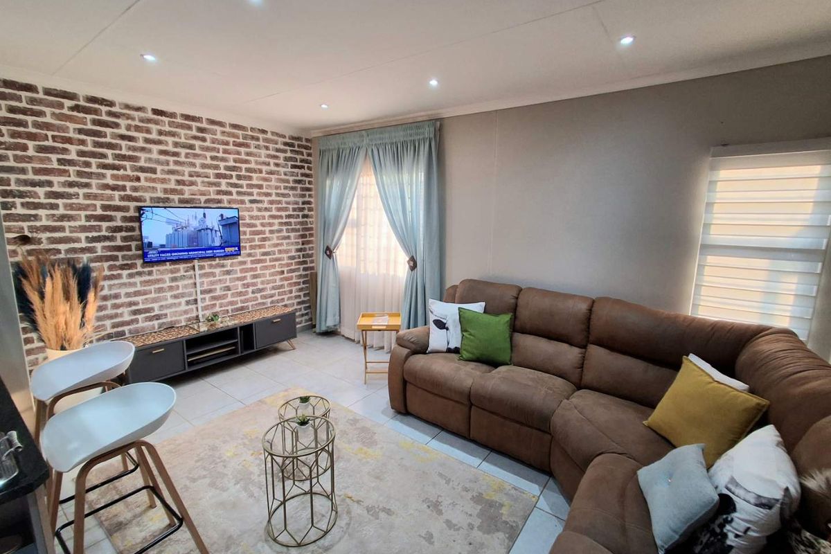 A well-maintained living room featuring an exposed brick accent wall, tiled flooring, and recessed downlighting, creating a warm and inviting atmosphere.