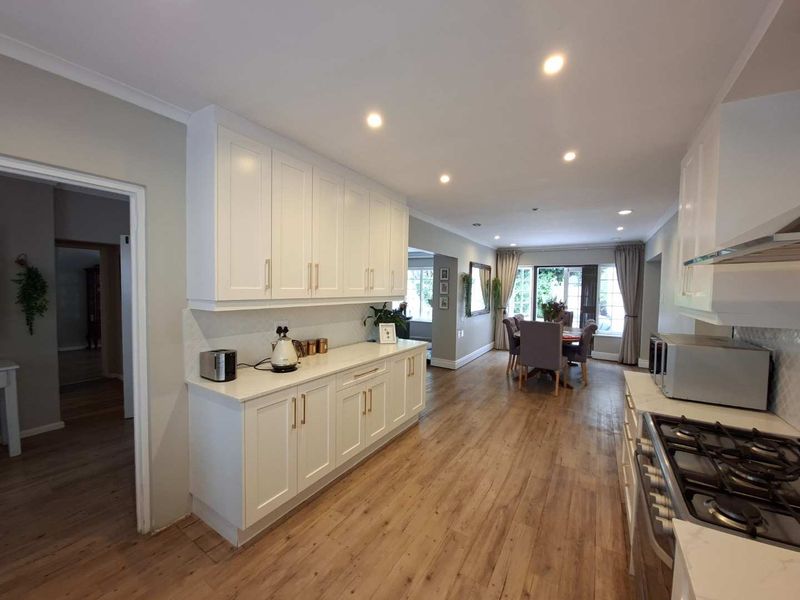 Spacious open-plan kitchen and dining area featuring modern white cabinetry, stone countertops, gas hob, and warm laminate flooring with recessed lighting.