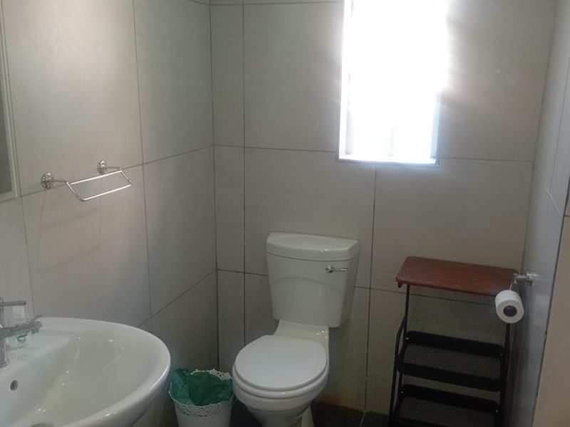 A functional bathroom featuring a pedestal basin, toilet, and neutral wall and floor tiling with a small window for natural light.