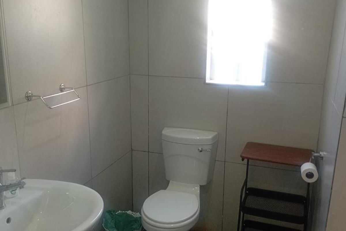 A functional bathroom featuring a pedestal basin, toilet, and neutral wall and floor tiling with a small window for natural light.