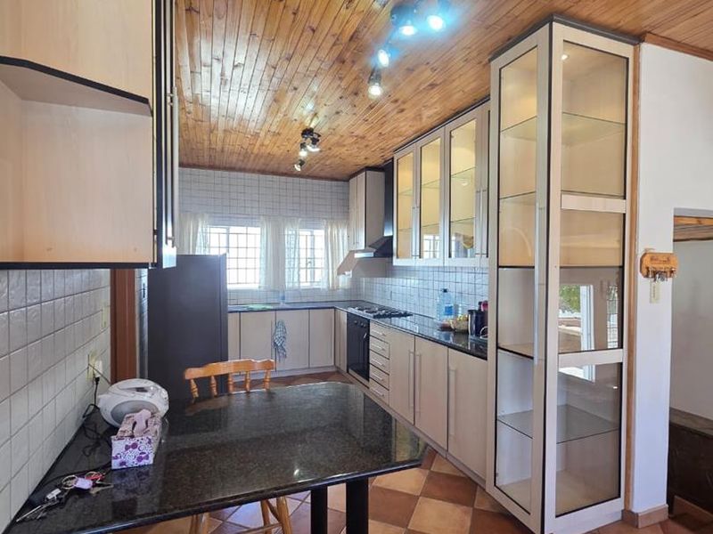 A functional kitchen featuring timber ceiling paneling, granite countertops, tiled backsplash, and ample built-in cabinetry with an integrated glass display unit.
