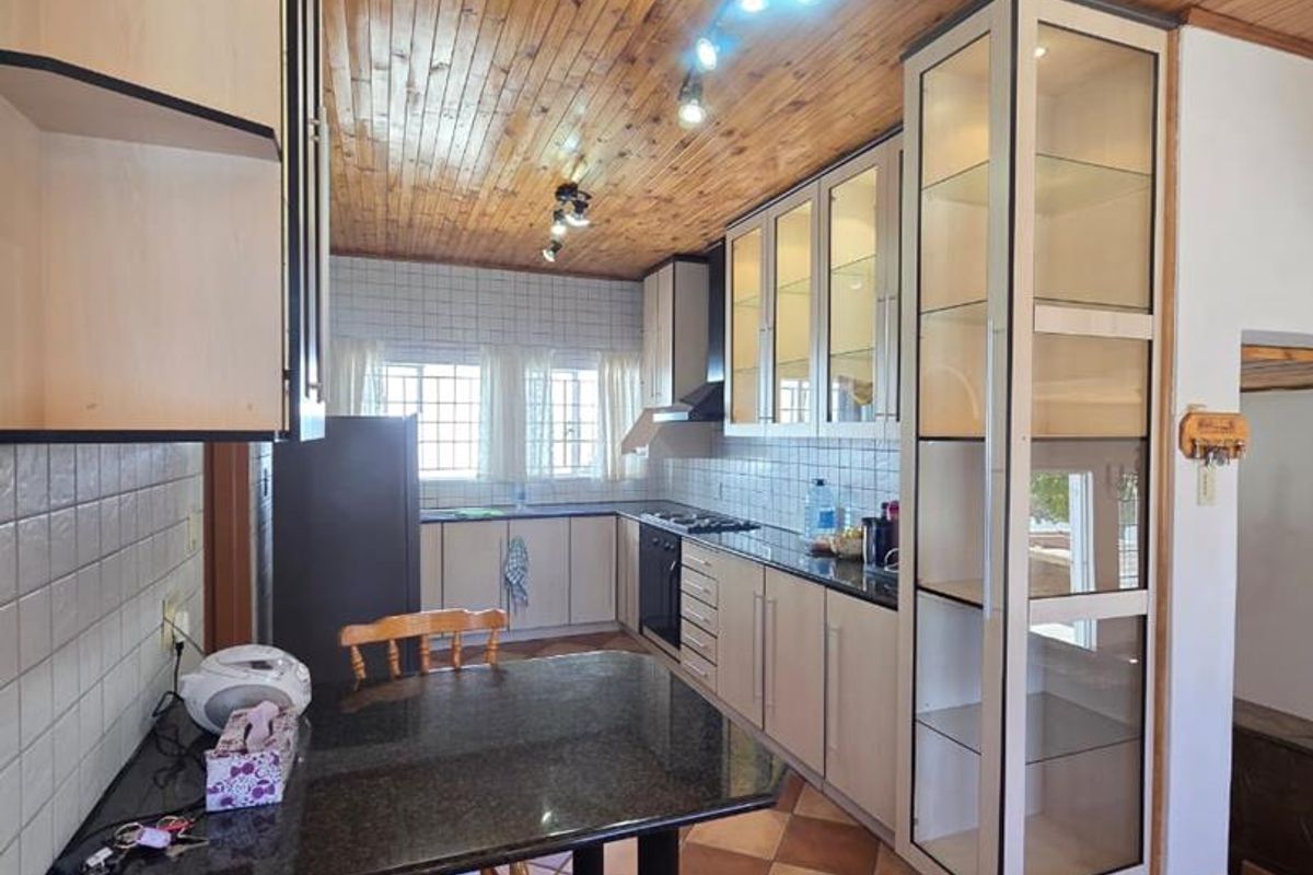 A functional kitchen featuring timber ceiling paneling, granite countertops, tiled backsplash, and ample built-in cabinetry with an integrated glass display unit.