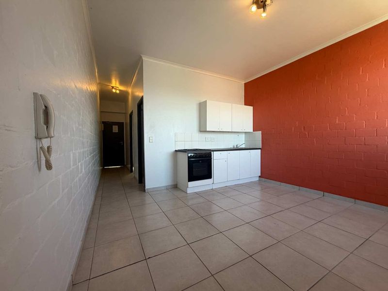 An open-plan living and kitchen area featuring tiled floors, a compact kitchenette with built-in oven, and a distinctive red brick feature wall.
