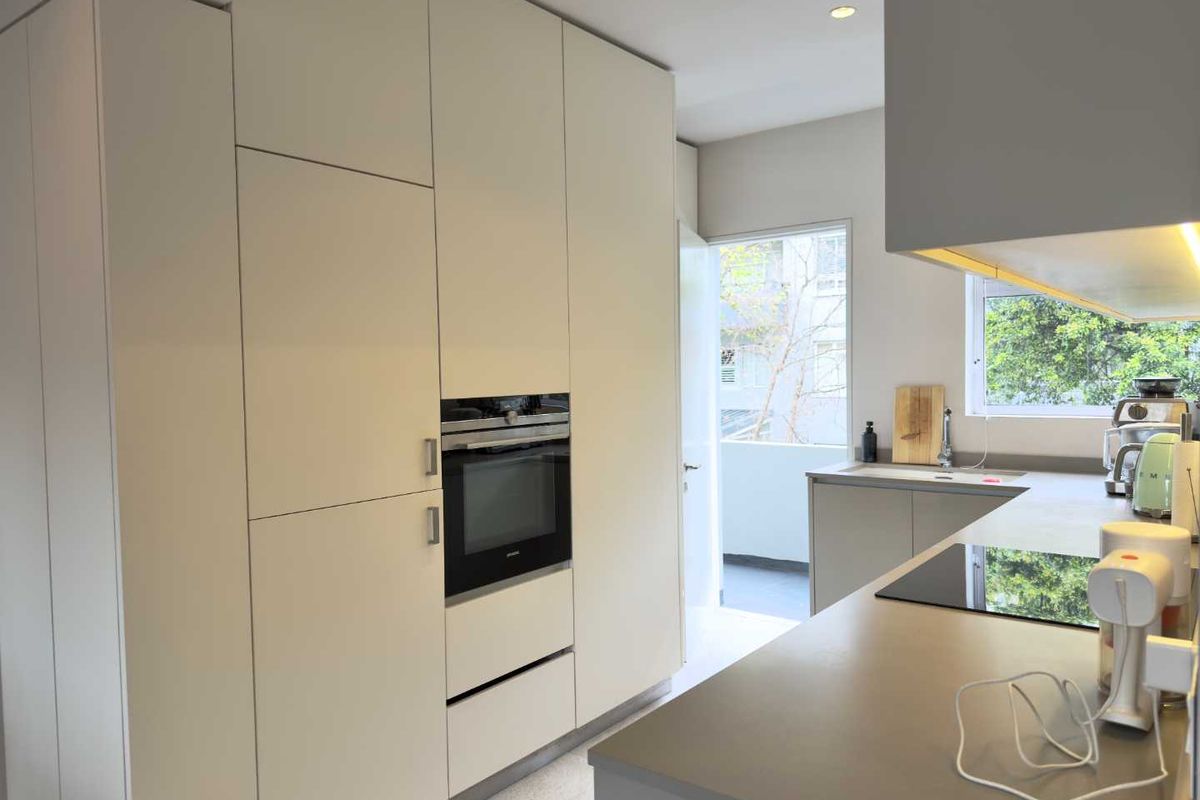 Modern kitchen featuring sleek integrated cabinetry, built-in oven, induction hob, and stone countertops with a clean, minimalist aesthetic.