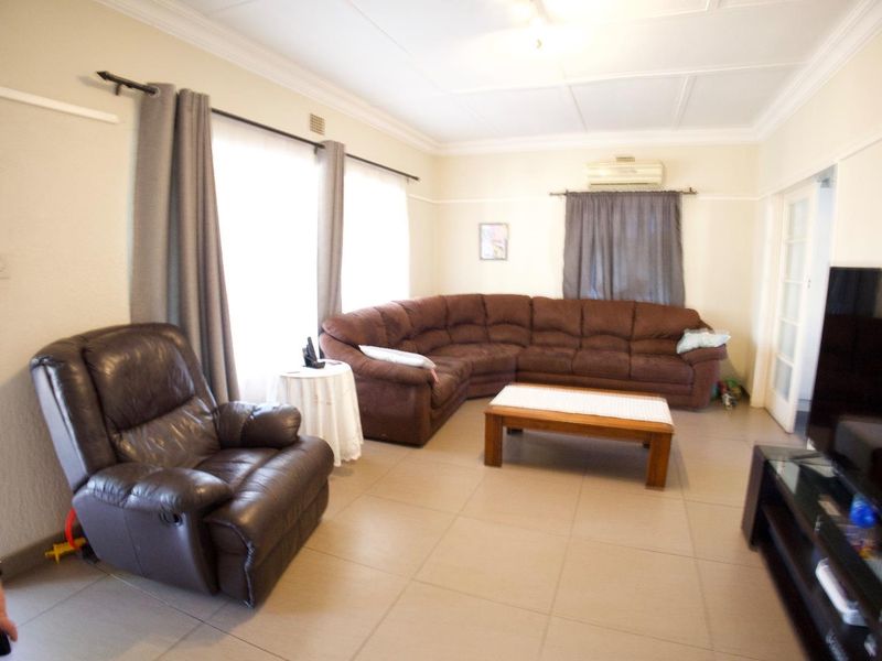 A spacious living room featuring neutral tiled flooring, decorative ceiling cornicing, and a wall-mounted air conditioning unit.