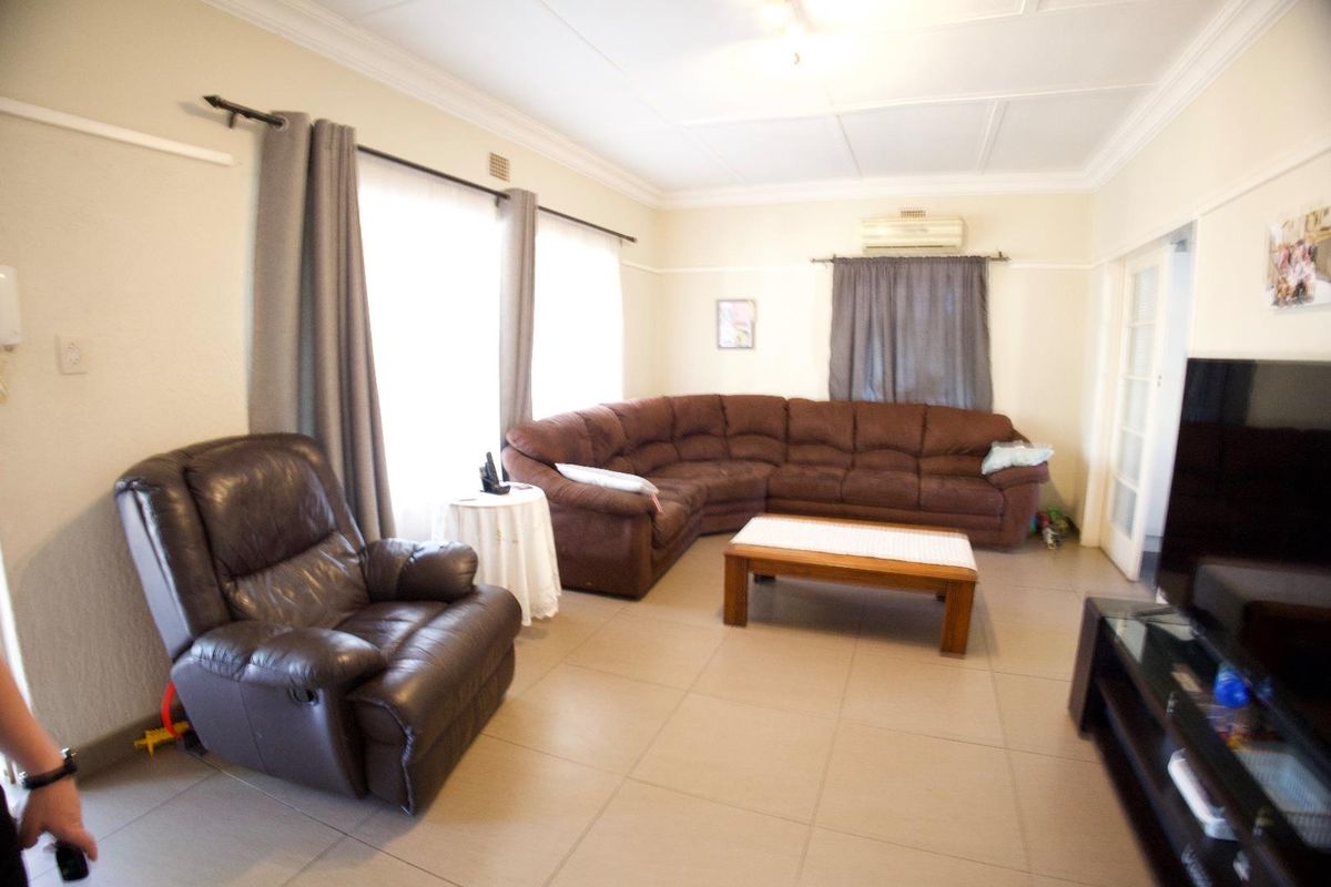A spacious living room featuring neutral tiled flooring, decorative ceiling cornicing, and a wall-mounted air conditioning unit.