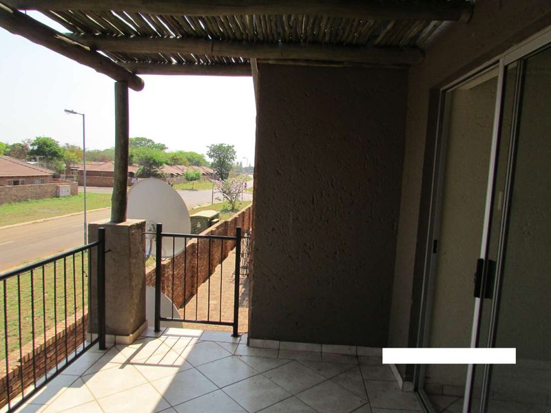 A covered balcony featuring tiled flooring, a thatched roof, and metal railings, offering an outdoor space with views of the surrounding neighborhood.