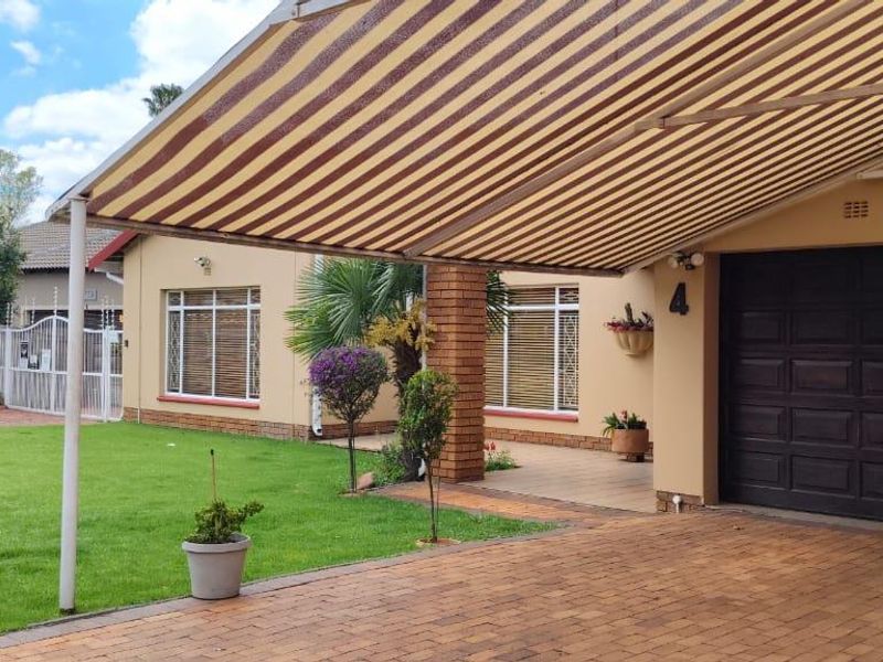 Front exterior view featuring a paved driveway, a large retractable striped awning, a garage entrance, and a well-maintained garden area.