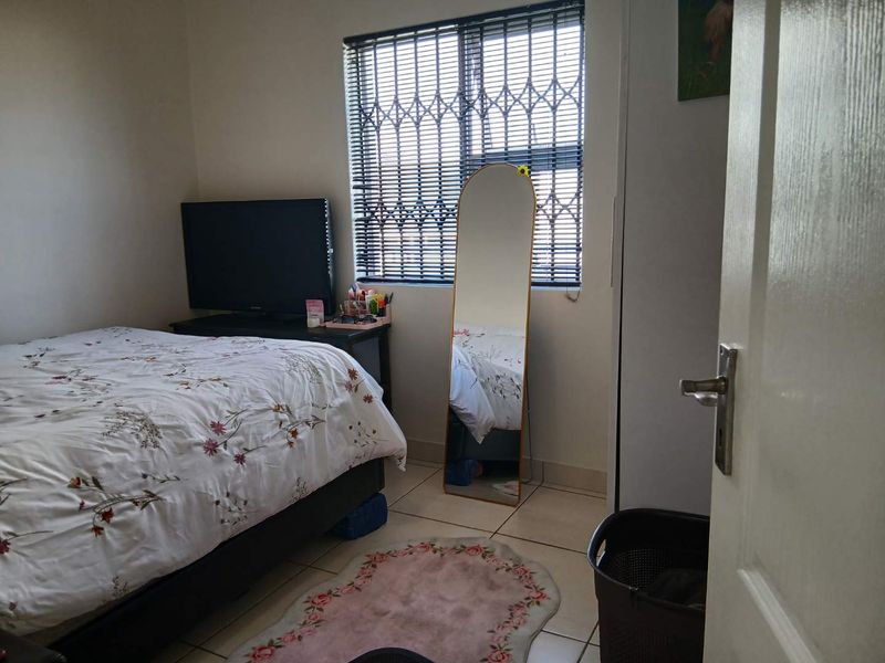 A functional bedroom featuring tiled flooring, a built-in cupboard, and a window fitted with security bars for added peace of mind.