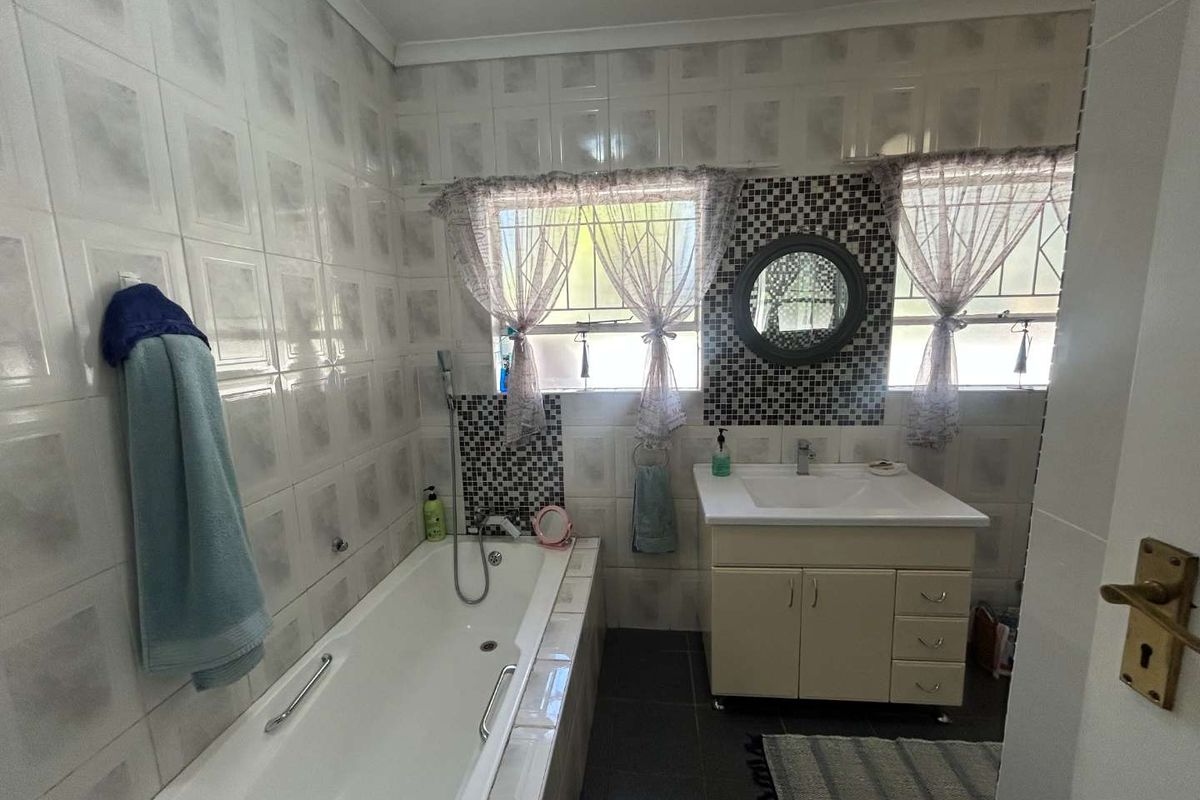 A functional bathroom featuring a built-in bathtub, vanity cabinet with basin, and tiled walls and flooring.