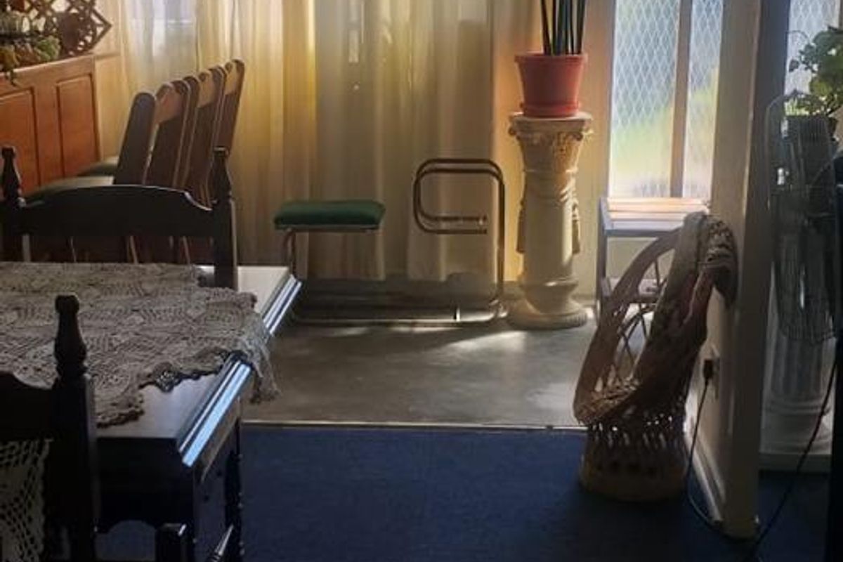 A living area featuring carpeted flooring and large windows with curtains, providing natural light and access to an adjacent outdoor space.