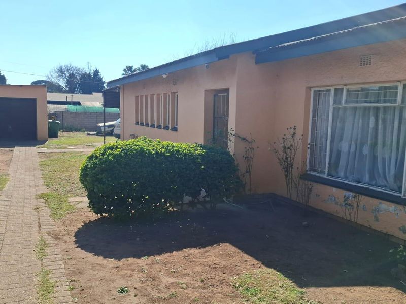 Rear view of the property featuring a detached garage, paved walkway, and exterior walls showing signs of wear and peeling paint.