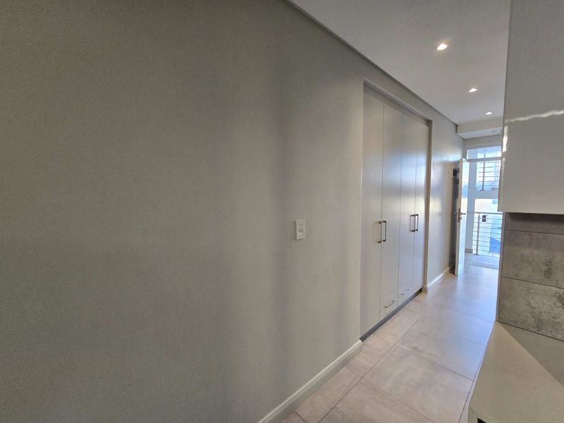 A clean, modern hallway featuring neutral tiled flooring, recessed downlighting, and ample built-in cupboard storage space.