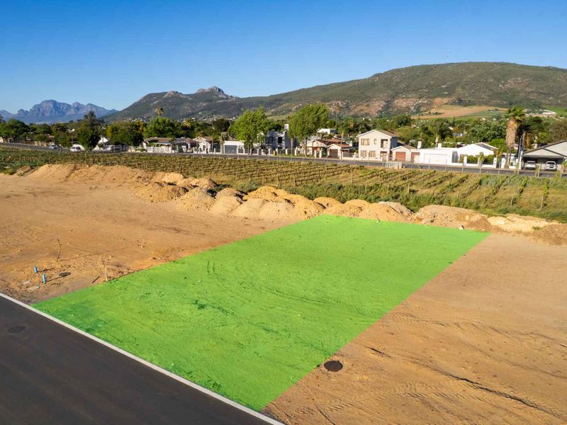 An aerial view of a vacant residential plot with road access, featuring a highlighted boundary and surrounding neighborhood landscape.