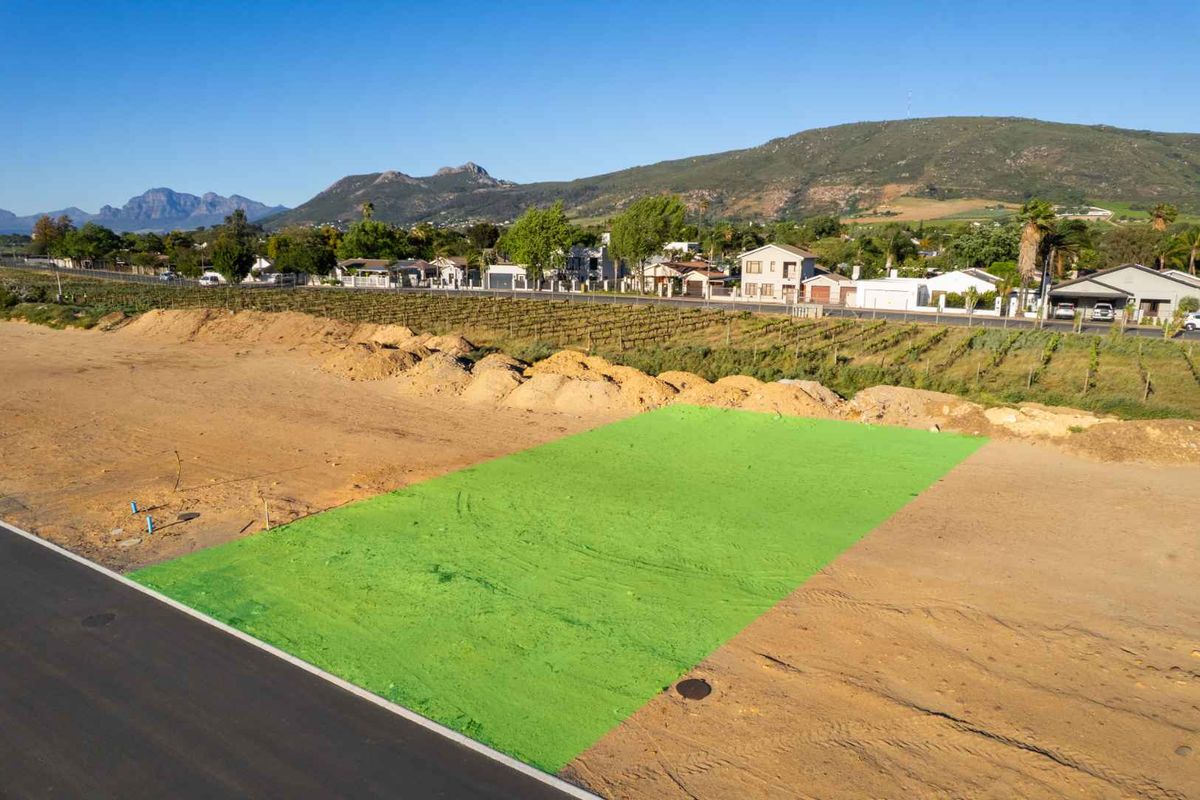 An aerial view of a vacant residential plot with road access, featuring a highlighted boundary and surrounding neighborhood landscape.