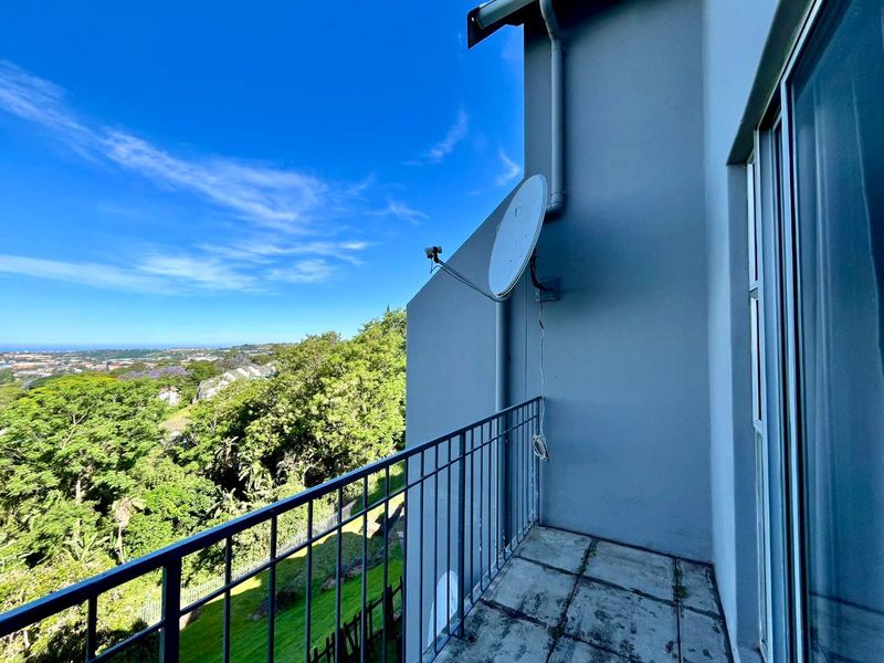 A balcony featuring metal railings and tiled flooring, offering an elevated view of the surrounding landscape and greenery.