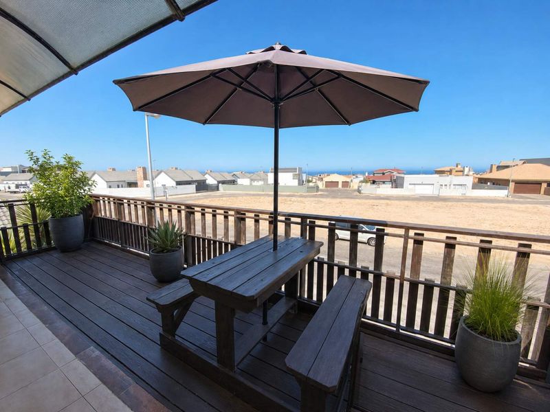 An elevated timber balcony featuring a protective roof covering and balustrade, offering an open outdoor space with neighbourhood views.