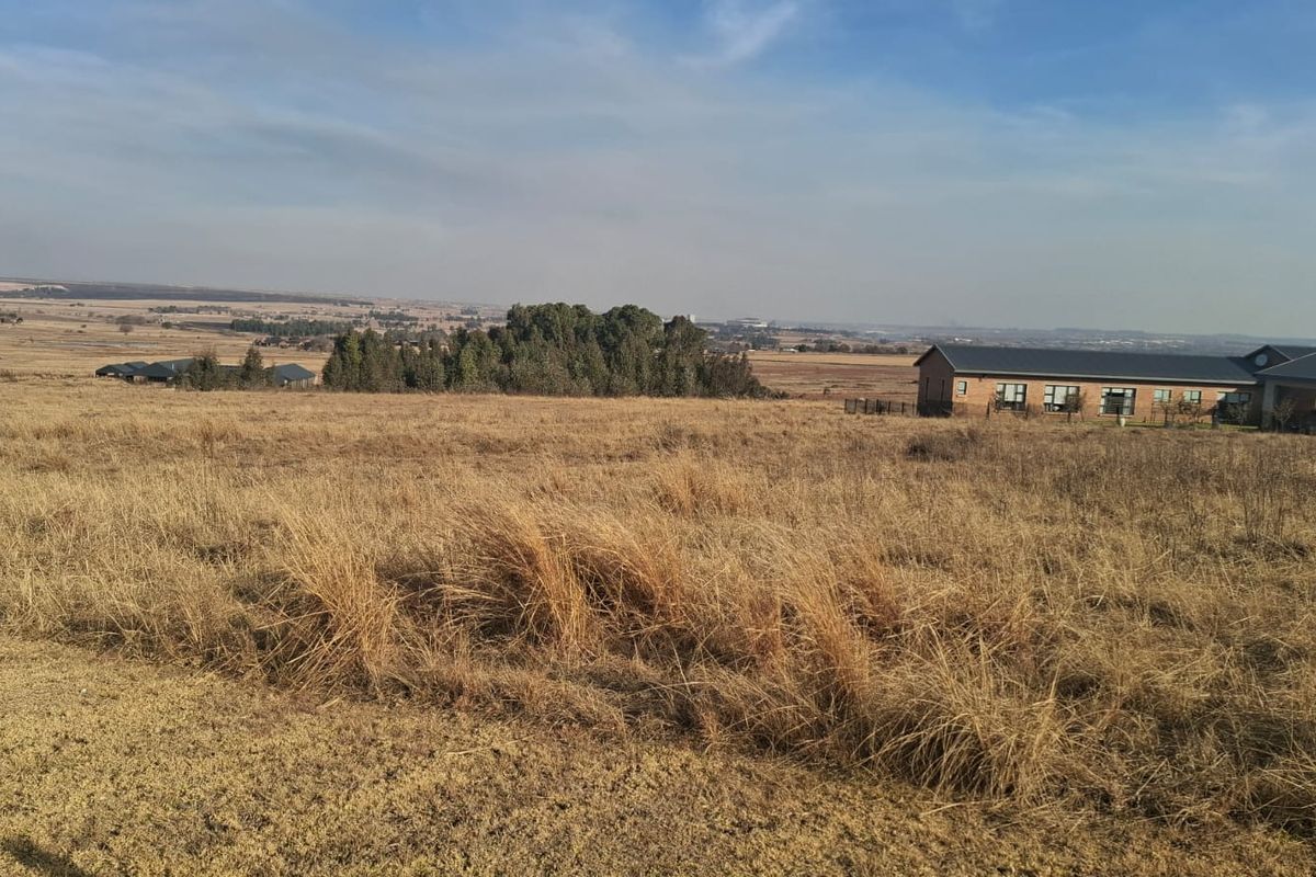 A wide-angle view of an expansive, undeveloped residential plot featuring natural grassland with distant neighboring properties visible on the horizon.