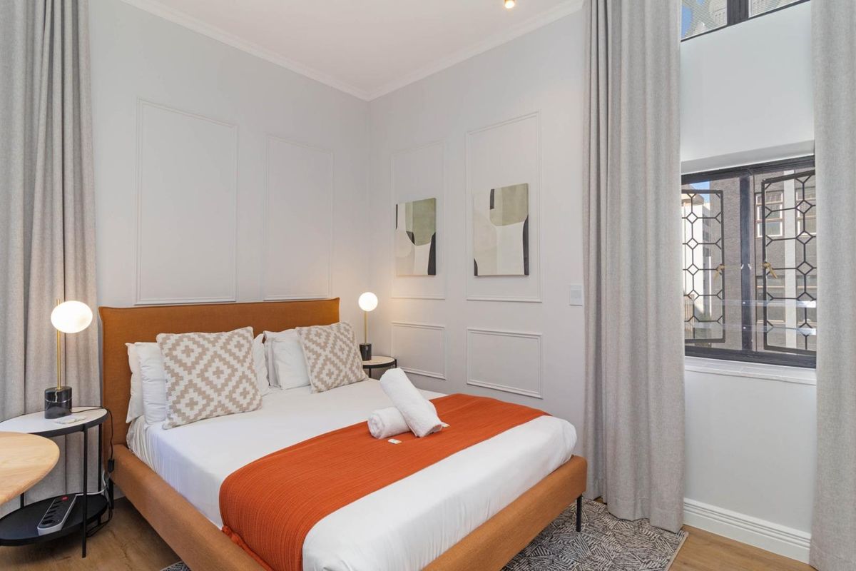 A well-maintained bedroom featuring decorative wall molding, neutral tones, and a window with security bars.