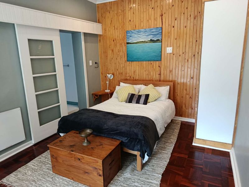 A bedroom featuring warm timber wall paneling, classic parquet flooring, and a sliding door providing access to an adjoining space.