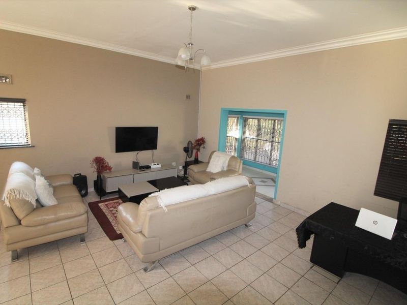A spacious living room featuring ceramic floor tiles, coved cornicing, and security bars on the windows, offering a functional and well-lit living space.