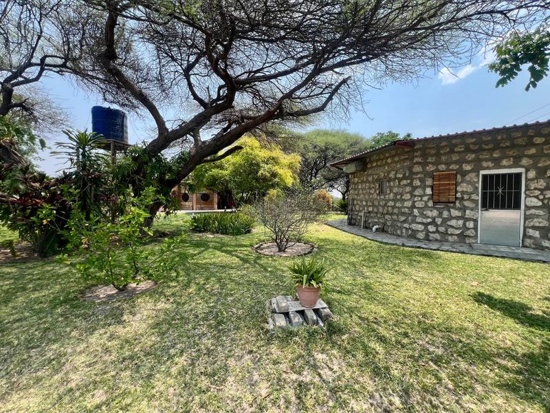 A view of the rear exterior featuring stone-clad walls, a metal security door, and a raised water storage tank set within a garden area.