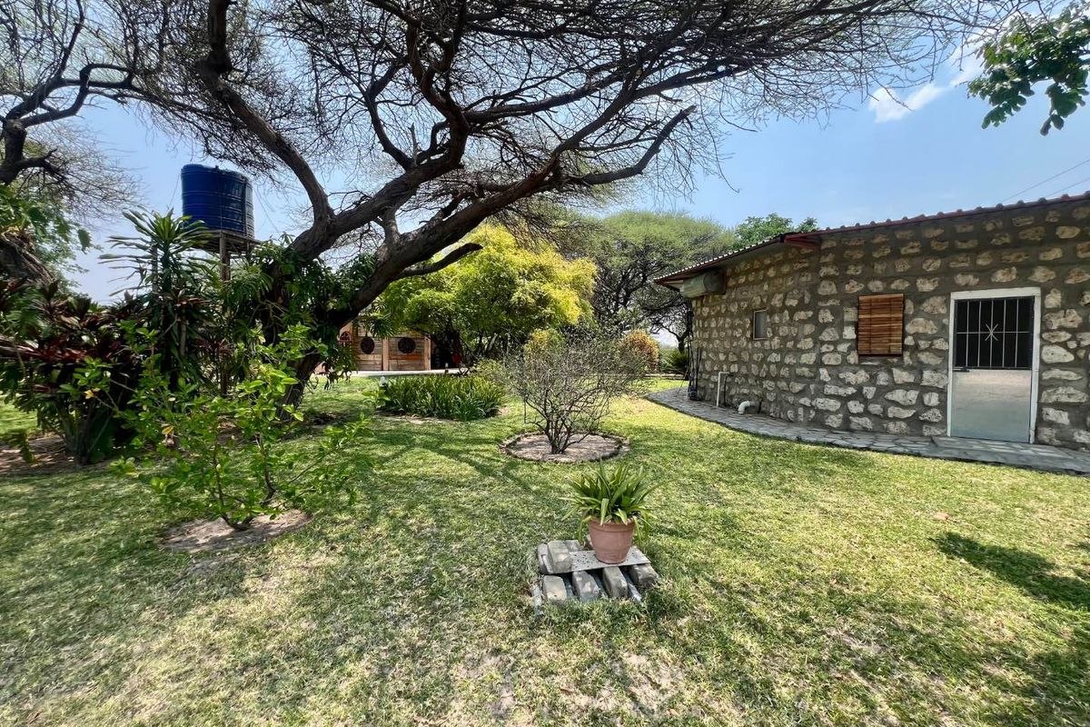 A view of the rear exterior featuring stone-clad walls, a metal security door, and a raised water storage tank set within a garden area.