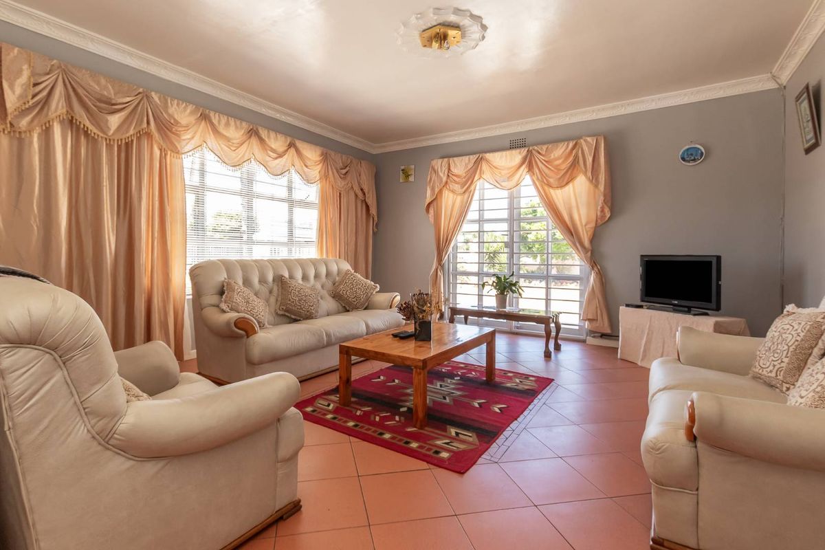 A spacious living room featuring terracotta floor tiles, decorative ceiling molding, and large windows with security bars.