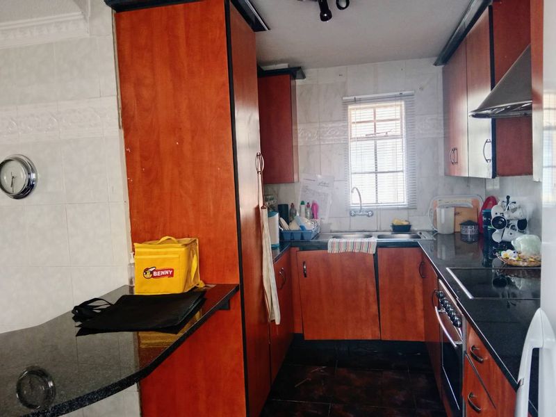 A functional kitchen featuring wood-finish cabinetry, dark granite countertops, a built-in oven, and an extractor fan with tiled finishes throughout.