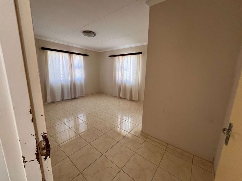 A vacant bedroom featuring neutral tiled flooring, large windows with curtain rails, and a simple ceiling light fixture.