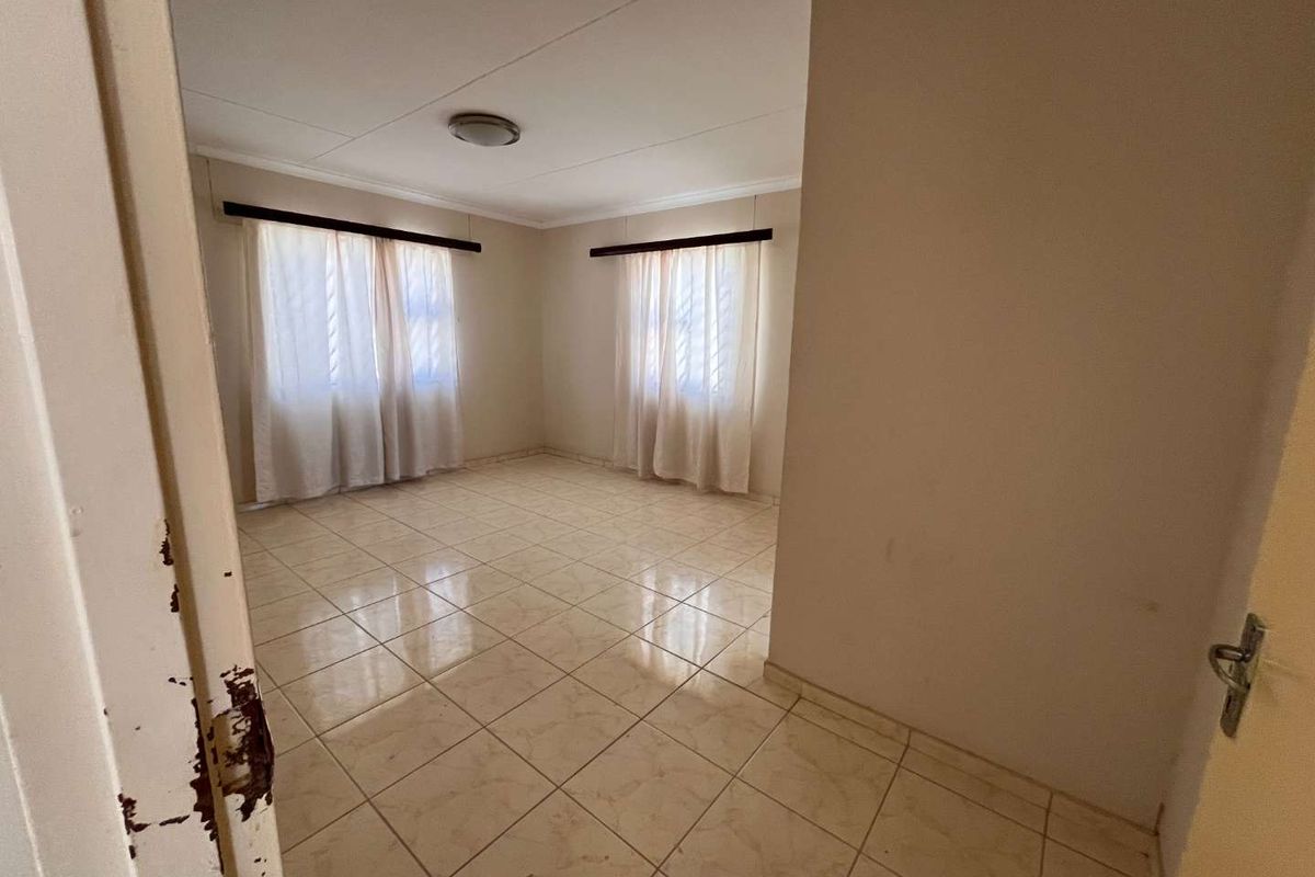 A vacant bedroom featuring neutral tiled flooring, large windows with curtain rails, and a simple ceiling light fixture.
