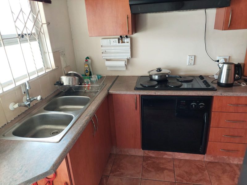 A functional kitchen featuring laminate countertops, a double bowl sink, built-in oven, electric hob, and extractor fan with tiled flooring.