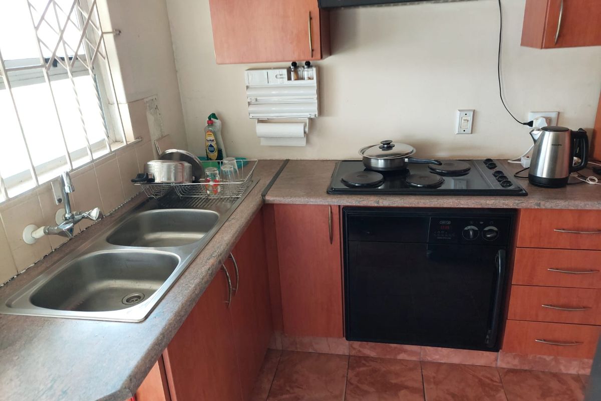 A functional kitchen featuring laminate countertops, a double bowl sink, built-in oven, electric hob, and extractor fan with tiled flooring.