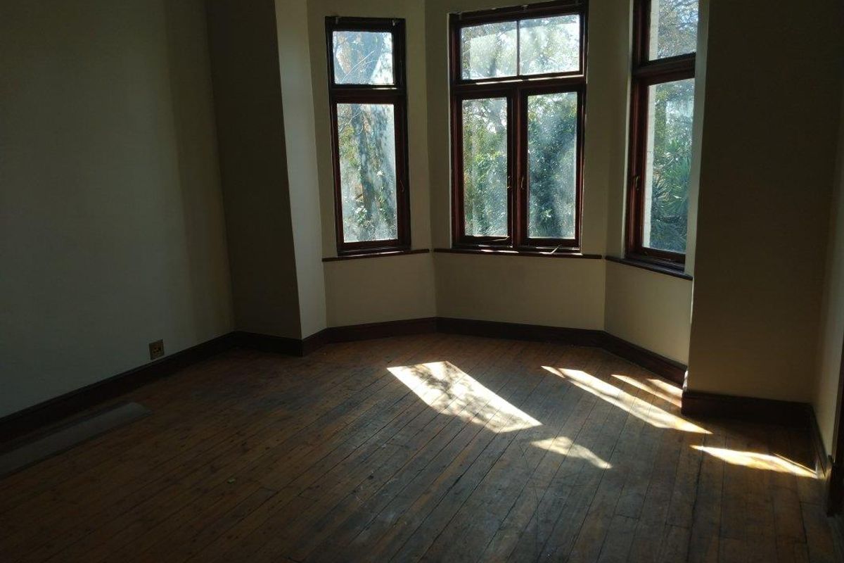 An empty bedroom featuring original timber flooring and a classic bay window with timber frames, offering a bright and character-filled space.