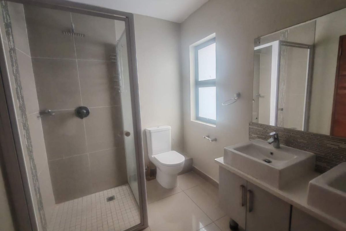 Modern bathroom featuring a glass-enclosed walk-in shower, dual vanity with basin, and tiled flooring.