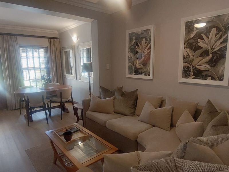 Open plan living and dining area featuring laminate flooring, crown molding, and natural light through a glass panel door.