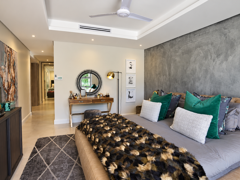 Spacious bedroom featuring a textured feature wall, recessed ceiling with integrated ducted air conditioning, ceiling fan, and neutral tiled flooring.