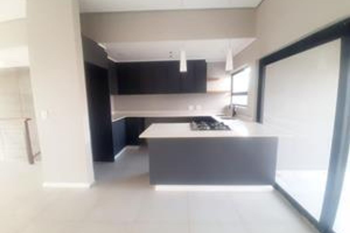 Modern open-plan kitchen featuring dark cabinetry, stone countertops, a central island with a built-in gas hob, and large sliding doors leading to the exterior.