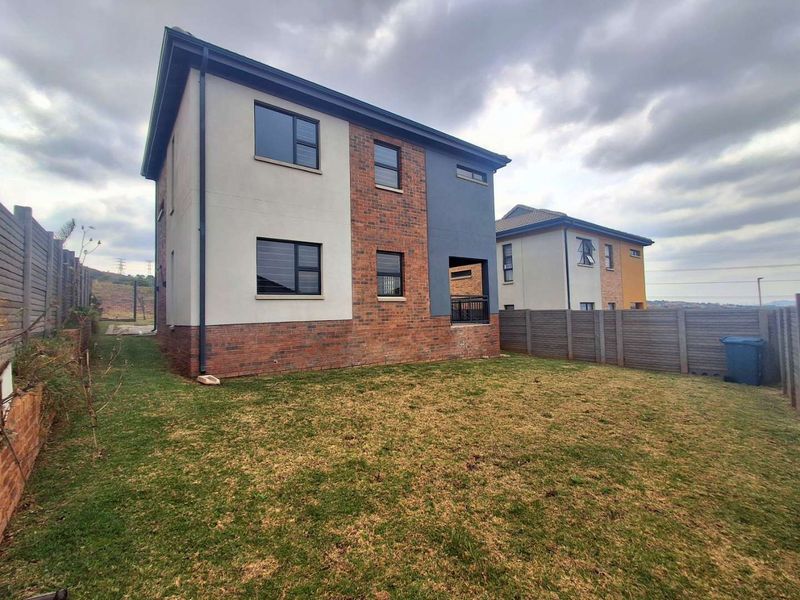 Rear view of a modern two-story house featuring a mix of brick and plastered finishes, aluminium windows, and a private backyard with boundary walling.
