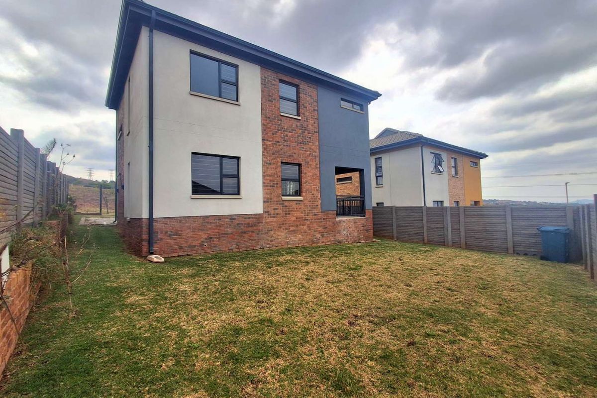Rear view of a modern two-story house featuring a mix of brick and plastered finishes, aluminium windows, and a private backyard with boundary walling.