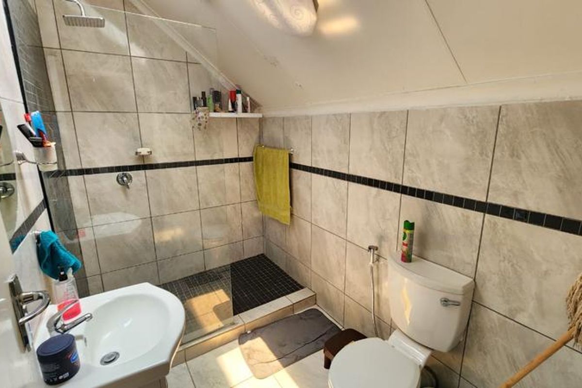 A compact bathroom featuring a walk-in shower with glass screen, pedestal basin, and toilet, finished with neutral wall tiles and a dark tiled shower floor.