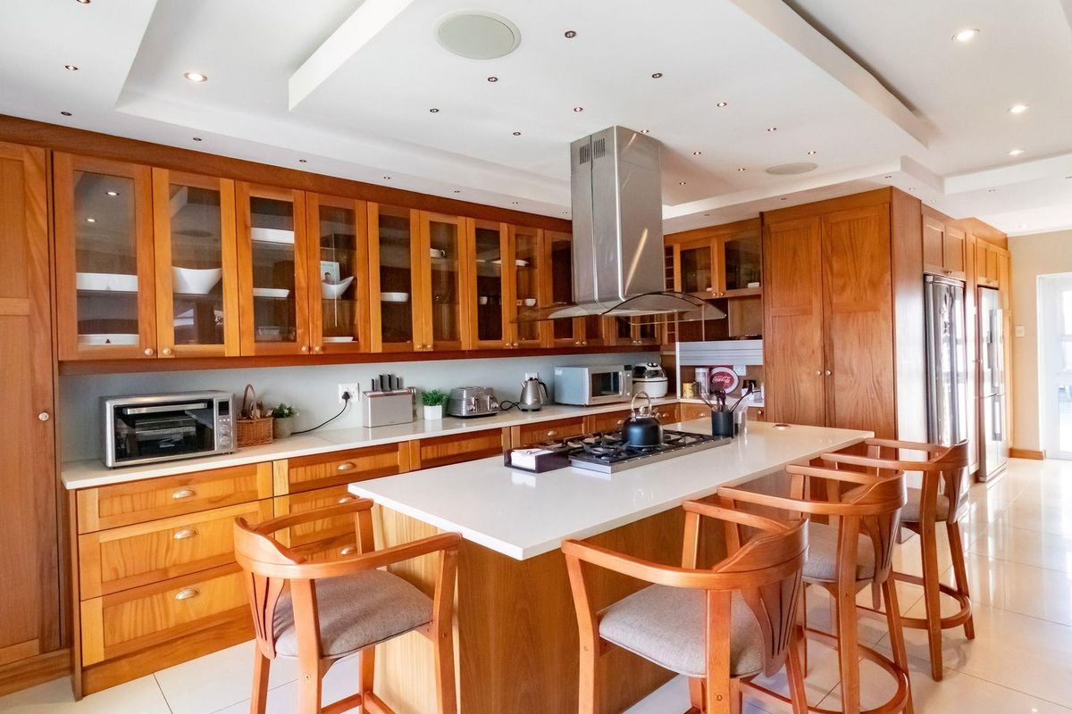 Spacious kitchen featuring warm timber cabinetry, a central island with a built-in gas hob, stainless steel extractor fan, and sleek stone countertops.